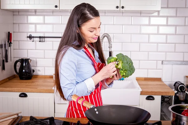 Ung kvinna förbereder broccoli i kök. Stockbild