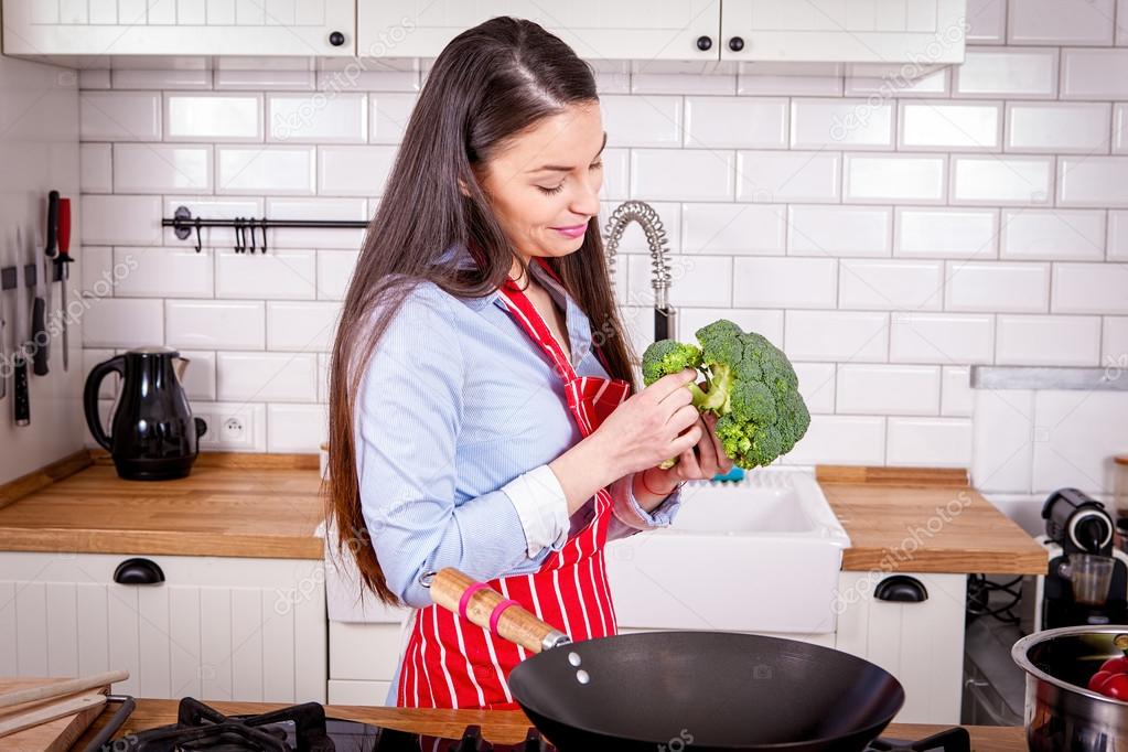 Young woman preparing broccoli in kitchen.