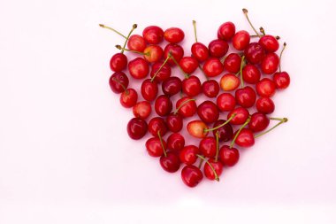 Açık pembe arka planda kalp şeklinde kırmızı kirazlar.