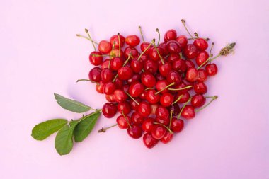 Kalp şeklindeki kırmızı kirazlar açık pembe arka planda yeşil dallı oklar..