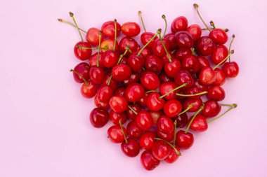 Açık pembe arka planda kalp şeklinde kırmızı kirazlar.