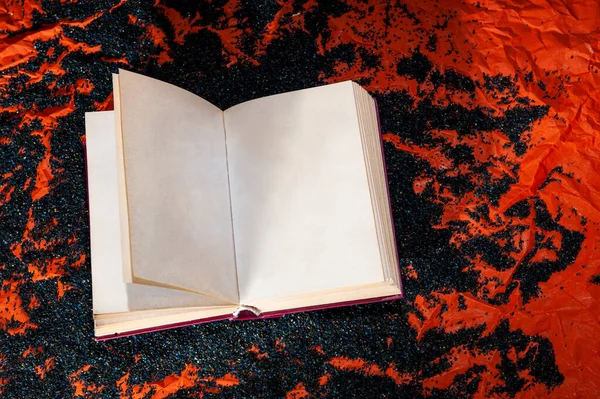 Opened book with printed text on loose powder of black color, with an orange background.