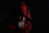 Chmurný muž středního věku s šedým vousem v kostkované červené plátěné bundě s kapucí na hlavě