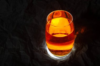 Bir kap, koyu bir zemin üzerinde parlak ışıklar ve renkler olan bir yığın kehribar sıvısı.