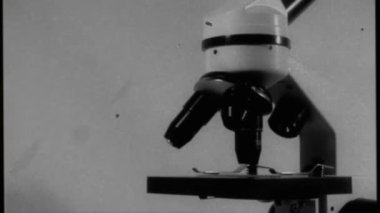 Aged video, filmed movement around a microscope with three black lenses and an instrument table