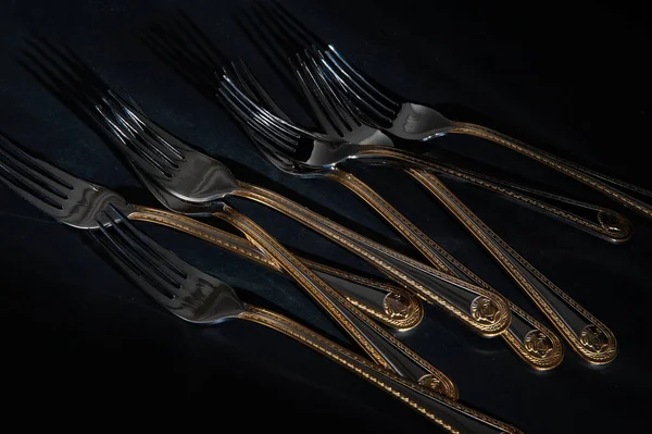 Forks, silver-colored metal cutlery with gold-colored handles on a dark background