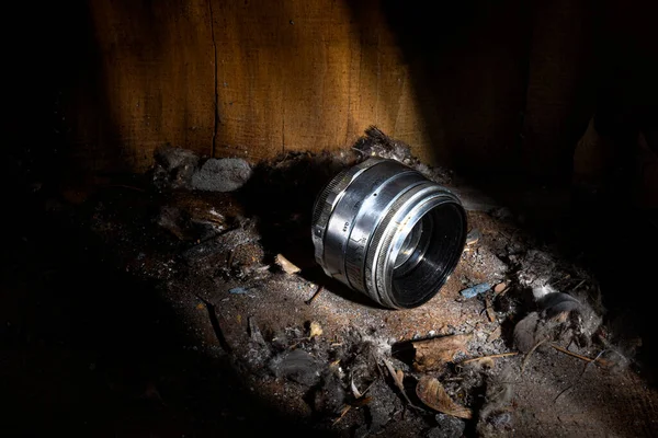 old lens on a pile of dirt and dust against the background of old walls made of hewn boards in a beam of light