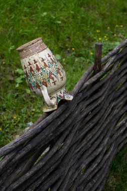 Ağaç dallarından örülmüş bir çitin üzerinde ulusal Batı Ukrayna desenli bir sürahi, kırık bir boyun parçası, kırsal bir bahçenin çitlerinde kurur.