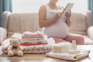 Hamile kadın doğumevi için hazırlanıyor, bebek eşyaları topluyor. Hamile bir kadın bebek kıyafetleri hazırlıyor ve planlıyor. Evdeki doğum hastanesi için hazırlık yapıyorum. Hastanedeki şeylerin listesi..