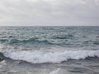 Deniz dalgaları köpükle kaplıdır. Deniz yüzeyinde köpük. Deniz dalgaları dalgalar ve köpüklerle kayalık deniz kıyısında kırılıyor..