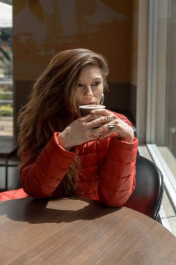 Güzel Latin bir kadın restoran masasında oturmuş elinde iki eliyle bir fincan kahve tutuyordu. Gün ışığında çekilmiş bir fotoğraf.
