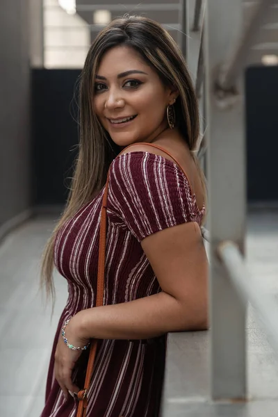 beautiful latin woman with long hair smiling and posing close to the wall, wears a jumpsuit, clothes in casual style in the city
