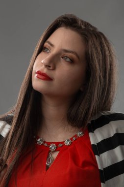 Uzun saçlı, makyajlı, kırmızı bluz ve ceket giyen, stüdyoda fotoğraf çeken beyaz tenli genç bir kadının yüzü.