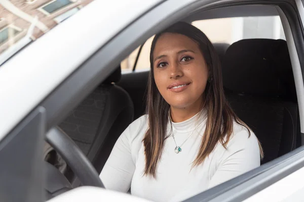 attractive latin woman with straight hair sitting inside a car in front of the wheel, smiling, lifestyle
