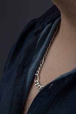 closeup of a thick silver necklace, wear a blue shirt, details of the textures, studio