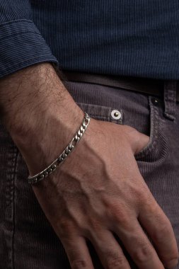 hand of a person in the pocket of his pants, uses a silver bracelet on his wrist, details of the textures