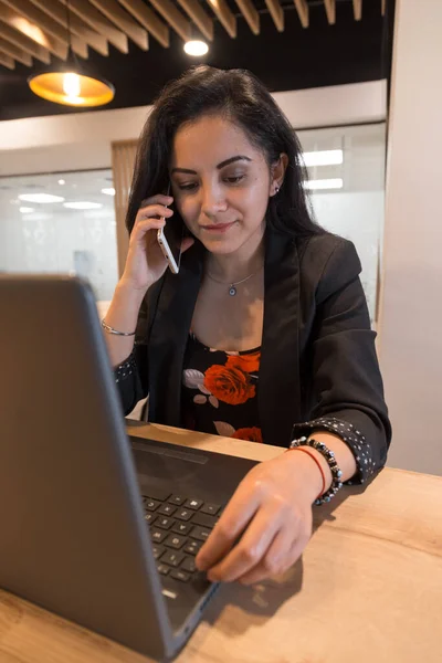 オフィスでパソコンや机の上の電話で仕事をしているエレガントな服を着た美しい女性少女が携帯電話で話します — ストック写真