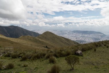 Dağların manzarası, bulutlu bir gökyüzü ve arka planda And Dağlarının ortasında bir şehir.