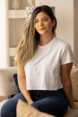 Uzun boyalı saçlı genç bir Latin kadın kanepede otururken gülümsüyor.