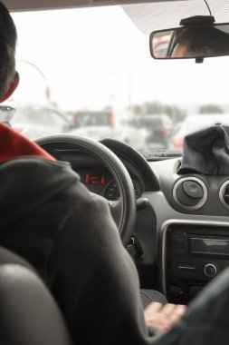 Bir arabanın içinde, direksiyon simidini, aynayı ve konsolu gösteren, trafikte araba kullanan bir kişi, detaylar