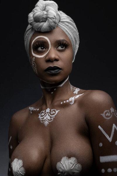 Detail of the face of an African American woman wearing makeup and painted figures on her face, wearing a scarf on her head, studio with gray background