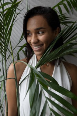 Gülümsemekten mutlu olan güzel bir esmer kadının yüzüne yakından bakın, bir bitkinin yaprakları var, kısa saçlı, beyaz bir bluzu, stüdyosu var.