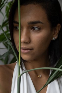 Bir bitkinin yapraklarının yanında güzel esmer bir kadının yüzünün ayrıntıları. Kısa saçları var, doğayla iç içe çalışıyor.