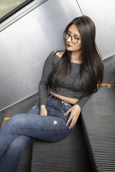 年轻的拉丁女模特 头戴眼镜 牛仔裤 头戴灰色休闲装 一头黑发 坐在楼梯上 享受生活方式 — 图库照片