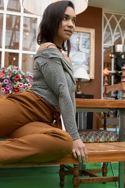 Latin woman with short black hair, is posing sitting on a wooden bench, wearing casual and comfortable clothes, fashion and lifestyle