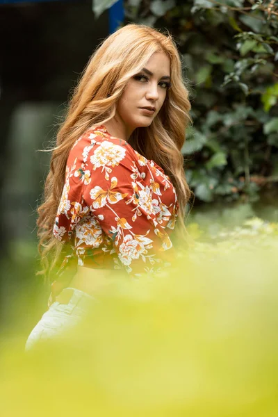 阳光明媚的日子里 有着一头金发的拉丁女人站在花园的植物旁边 穿着休闲装 生活方式和自然 — 图库照片