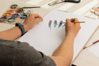 Boş çarşaflı bir çalışma kitabına resim yaparken fırça tutan kişi, iş yerinde paletli bir masa, yaratıcılık ve sanat eserleri, el sanatları objeleri