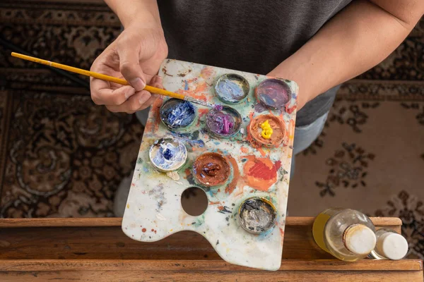 油絵具 工作道具 スタジオでの創造的なライフスタイルに近いブラシでパレットの上の色を混合しながら 芸術家の手の塗料の完全な作業 — ストック写真