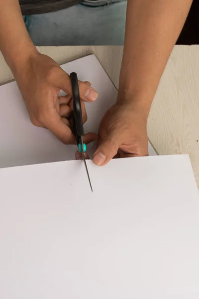 detail of person's hand cutting a blank paper with scissors on a desk, work tools for crafts, art and creativity with crafts