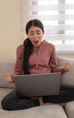 Genç bir kadın bilgisayarına bakarken çığlık atıyor, yoğun stres ya da öfke belirtileri gösteriyor. Bugünün dijital dünyasında aşırı duygusal yüklenme yakalar.