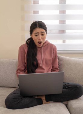 Kanepede oturan genç bir kadın bilgisayarına bakarken hayal kırıklığı içinde bağırıyor. Modern yaşamda öfke, stres veya çevrimiçi sorunları temsil eder..