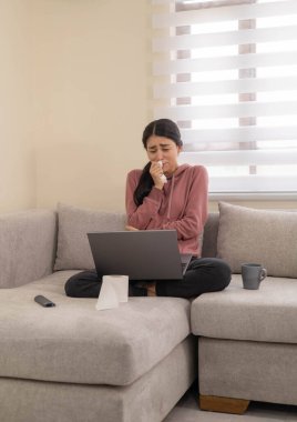 Genç bir kadın dizüstü bilgisayarını kullanırken endişeli bir ifadeyle kanepede oturuyor. Stres, kötü haber ya da dijital hayattaki duygusal rahatsızlığı temsil eder..