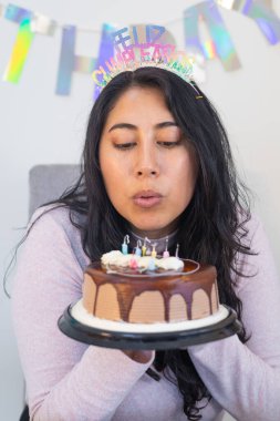 Pastanın üzerindeki mumu üflerken etrafı yemek ve süslemelerle çevrili bir kadın doğum günü dileği diliyor..