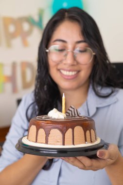 Sıcak bir evde doğum günü kutlaması sırasında masada elinde pasta ve aperatiflerle gülümseyen kadın..