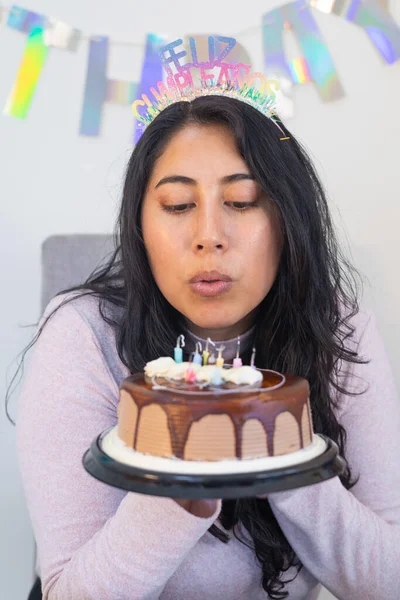 Pastanın üzerindeki mumu üflerken etrafı yemek ve süslemelerle çevrili bir kadın doğum günü dileği diliyor..