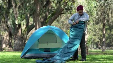 Ormanda huzurlu bir sabah çadırın yanında uyku tulumunu düzenleyen bir kampçı.