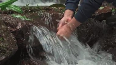 Nehirde ellerini yıkayan bir adamın yakın çekimi. Sadece elleri ve kolları görünüyor, tazeliği, sakinliği ve doğal saflığı vurguluyor..