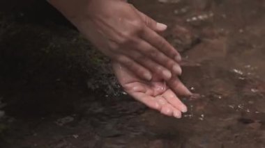 Temiz bir nehirde ellerini yıkayan bir kadının sakin bir hareketi ve doğal tazeliği ön plana çıkardığı yakın çekim videosu..