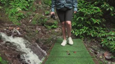 Kırsal ahşap bir köprüden geçen bir kızın videosu. Önden bakıldığında, doğayla çevrili küçük bir derenin üzerinden geçerken vücudunun alt kısmına odaklanıyor..