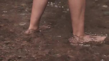 Kasık kemiğinden aşağısına odaklanmış bir video, sakin bir ormanda çıplak ayakla sığ bir nehre doğru yürüyen bir kadının hafif dalgalar oluşturduğunu gösteriyor..