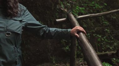Orman merdivenlerinden inerken ahşap bir tırabzanı kavrayan bir kadının yakın plan fotoğrafı. Hareket, istikrar ve etrafındaki doğal ortamı ön plana çıkarıyor..