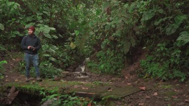 İzi yavaşça yürür, kamerasını kaldırarak manzarayı yakalar ve doğayla huzurlu bir anın tadını çıkarır..