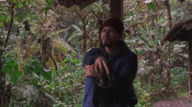 Genç bir adam kamerasıyla boş boş dinleniyor, bereketli doğal manzarayla çevrili kırsal bir barınağın huzurlu manzarasının tadını çıkarıyor..