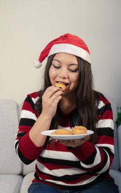 Evde dinlenirken kurabiye yiyen genç bir kadın. Elinde bir tabak dolusu fırınlanmış ikramla..