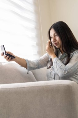 Kanepede oturup ev ortamında akıllı telefonuna bakan bir kadının sıradan bir portresi..