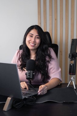 Bilgisayarının önündeki sanal konferans sırasında masa başı mikrofona konuşan genç bir kadın, çevrimiçi eğitimi, profesyonel iletişimi ve uzaktan sunumları temsil ediyor.
